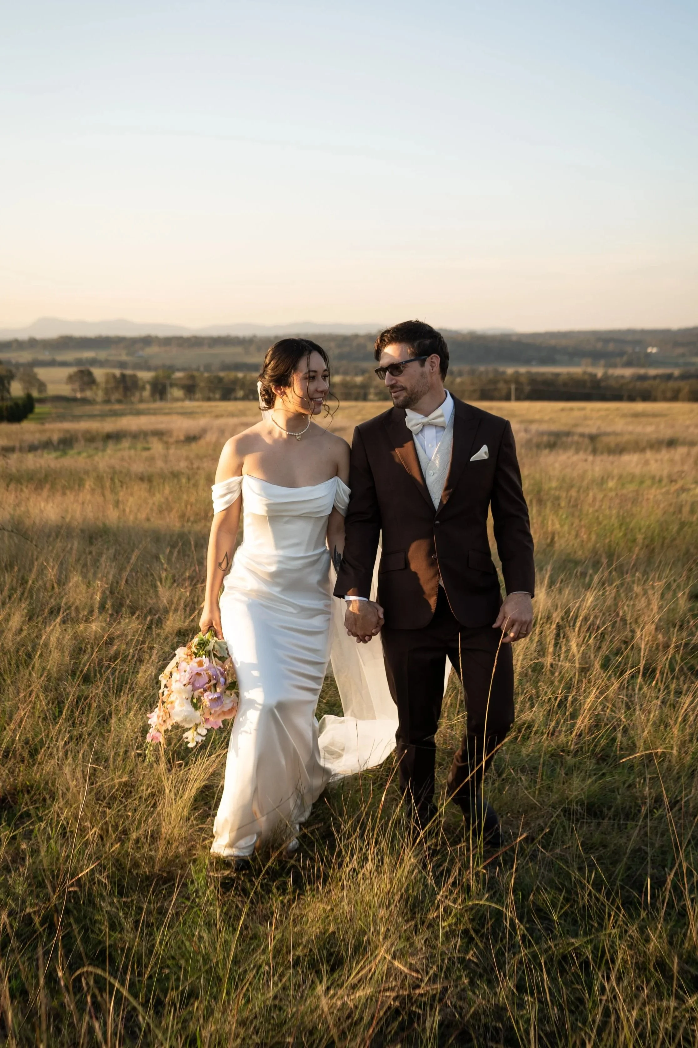 The couple walking through long grass at sunset