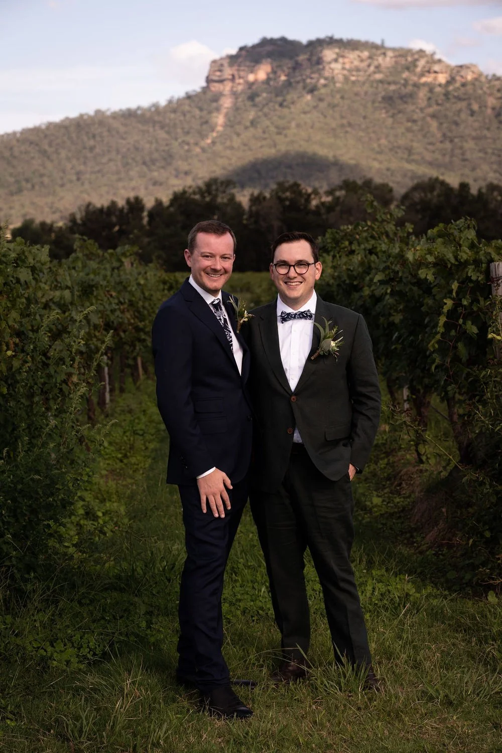 The couple in the vines with the mountains behind. Aaron & Scott's wedding at Margan Wines, Hunter Valley