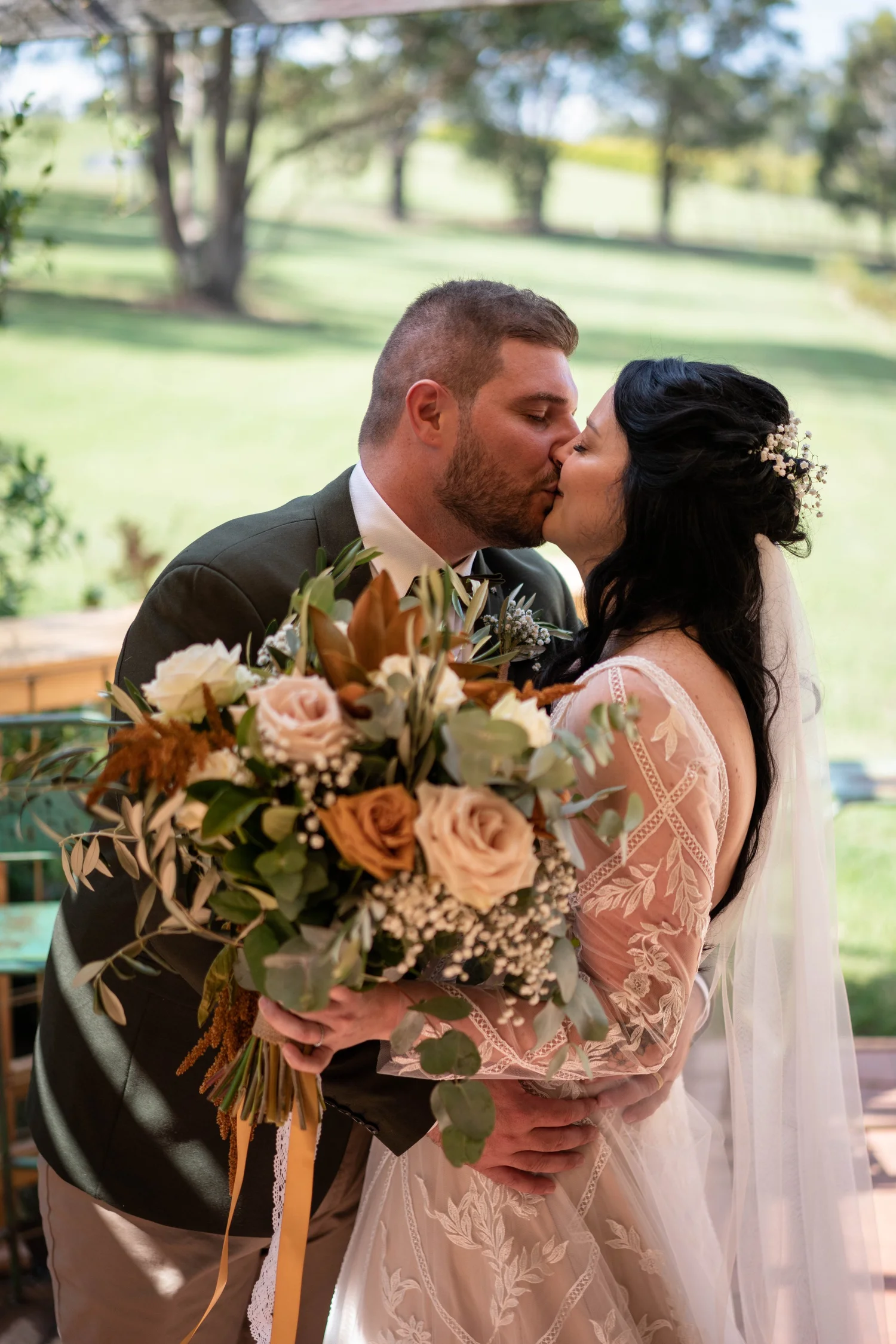 A kiss with the bouquet in the paddock. Alana & Peter's wedding at Peppers Creek, Hunter Valley