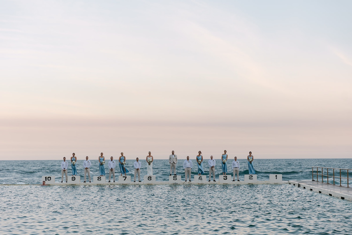 The wedding party lined up along the ocean baths. Jasmin & Jye's wedding at Merewether Surfhouse & Ocean Baths, Newcastle