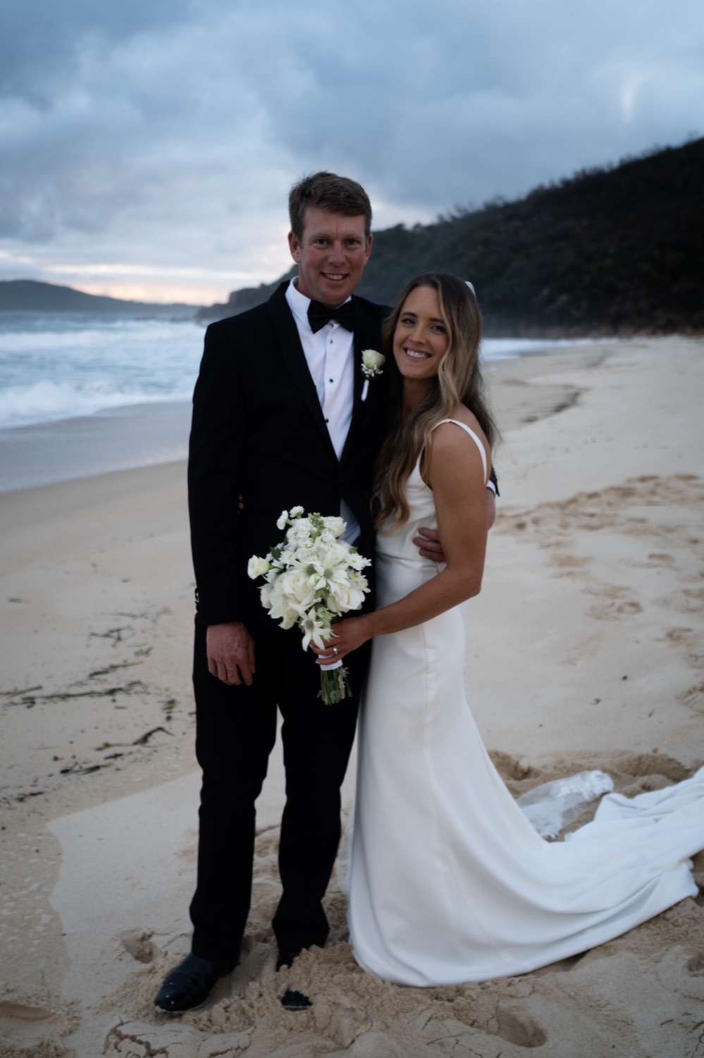 The couple on the beach with the headland behind. Lauren & Alasdair's wedding at Shoal Bay Beach, Port Stephens