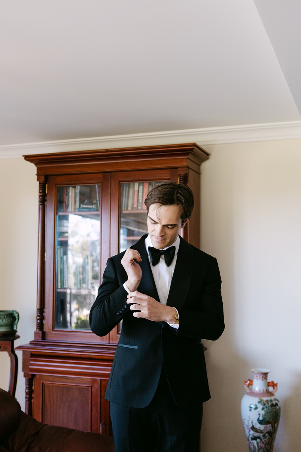 Getting ready in a tuxedo beside an antique cabinet. Phoebe & Cameron's wedding at Curzon Hall, Sydney